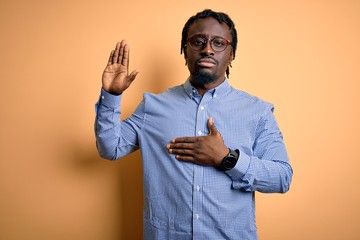 Young handsome african american man wearing shirt and glasses over yellow background Swearing with...