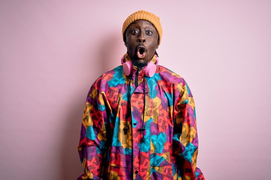 Young handsome african american man wearing colorful coat and cap over pink background afraid and shocked with surprise expression, fear and excited face.