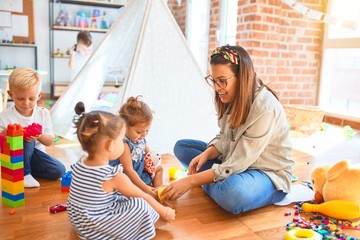 Beautiful teacher and group of toddlers playing around lots of toys at kindergarten