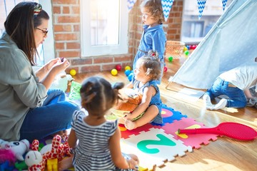 Beautiful teacher and group of toddlers playing around lots of toys at kindergarten