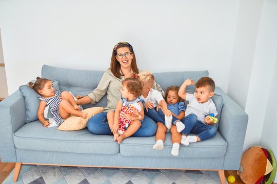 Beautiful teacher and group of toddlers sitting on the sofa playing at kindergarten