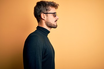 Young man wearing thug life fanny sunglasses standing over isolated yellow background looking to...
