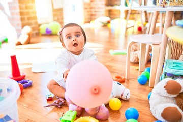 Beautiful infant happy at kindergarten around colorful toys