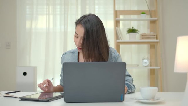 Slow Motion Normal Shot Zoom Out : Asian Woman Working At Home By Computer Laptop And Digital Tablet. Asia Freelance Girl Feeling Happy And Using Technology Device At Home. 