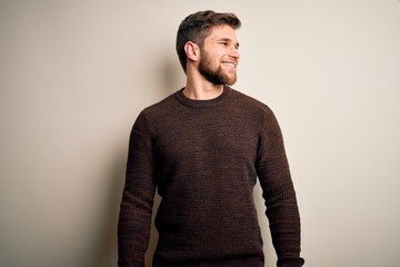 Young handsome blond man with beard and blue eyes wearing casual sweater standing looking away to...