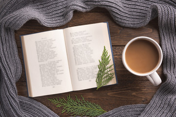 Flatlay composition with white knitted scarf, cup of coffe and open book on wooden desk table. Hygge style, cozy autumn or winter holiday concept. Flat lay, top view, overhead.