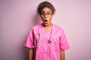 African american nurse girl wearing medical uniform and stethoscope over pink background afraid and shocked with surprise expression, fear and excited face.