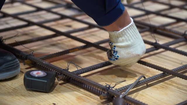 Man wear white gloves collects grid from metal fittings, connects two parts with jumpers, screws wire on factory close up. Worker measures distance between armature on wooden floor with roulette.