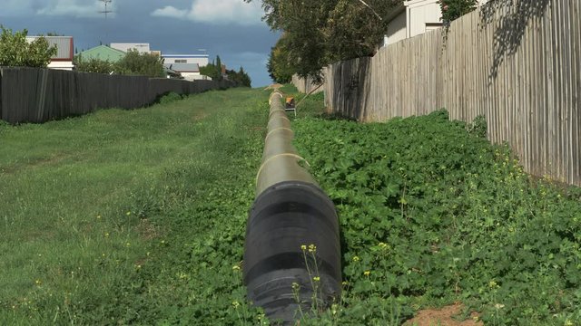 TILT UP Of Large Water Pipeline Down A Grassy Avenue In A Suburb