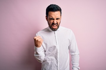 Fototapeta premium Young handsome man with beard wearing casual shirt standing over pink background angry and mad raising fist frustrated and furious while shouting with anger. Rage and aggressive concept.