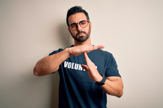 Handsome man with beard wearing t-shirt with volunteer message over white background Doing time out gesture with hands, frustrated and serious face