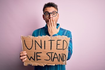 Young handsome activist man asking for union holding banner with united stand message cover mouth...