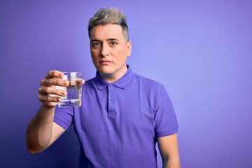 Young modern man drinking a glass of fresh water over purple isolated background with a confident expression on smart face thinking serious