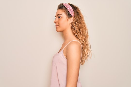 Young beautiful woman with blue eyes wearing casual t-shirt and diadem over pink background looking to side, relax profile pose with natural face with confident smile.