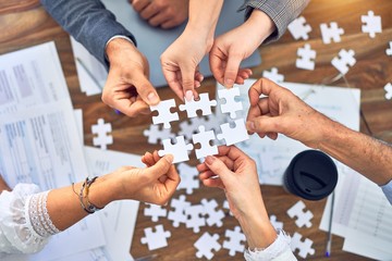 Group of business workers with hands together connecting pieces of puzzle at the office - obrazy, fototapety, plakaty