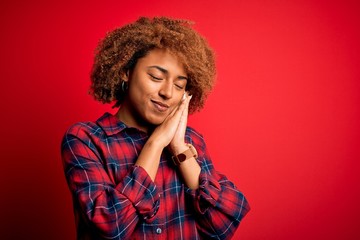 Young beautiful African American afro woman with curly hair wearing casual shirt sleeping tired dreaming and posing with hands together while smiling with closed eyes.