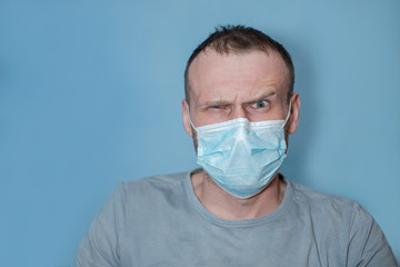 man in protective medical mask raised eyebrow in surprise. Angry man on blue background.