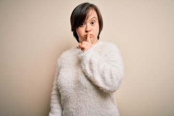 Young down syndrome woman standing over isolated background asking to be quiet with finger on lips. Silence and secret concept.