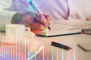 Double exposure of man's hands writing notes of stock market with forex chart.