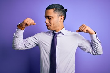 Young brazilian businessman wearing elegant tie standing over isolated purple background showing arms muscles smiling proud. Fitness concept.