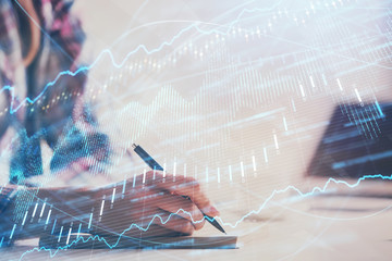 A woman hands writing information about stock market in notepad. Forex chart holograms in front. Concept of research. Double exposure