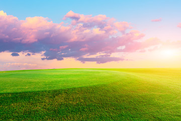 Green grass field and colorful sky clouds at sunset.