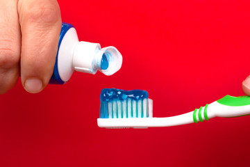 hand squeezes toothpaste on a toothbrush on a red background close-up. caries prevention and oral...