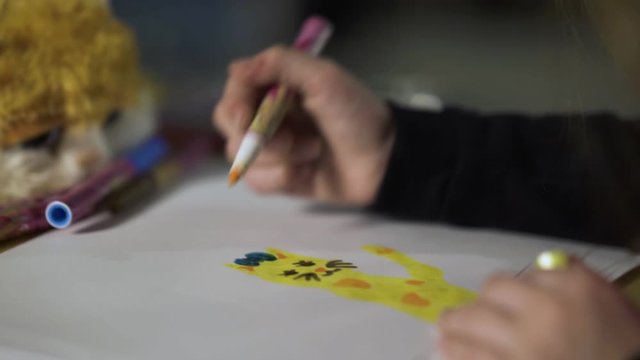 A young girl draws a cartoon kitten on paper table with colored pencils . Children's creativity. 4K