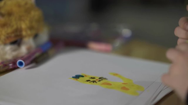 A young girl draws a cartoon kitten on paper table with colored pencils . Children's creativity. 4K