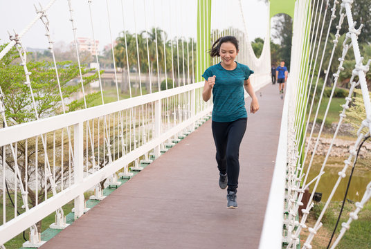 Beautiful Asian long hair women running over bridge at public park.Athletic woman jogging in evening time.Workout wellness and healthy lifestyle concept.
