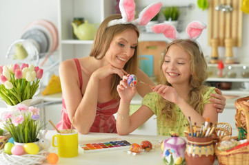 Mother with daughter wearing rabbit ears decorating Easter eggs at home