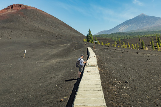 Young traveler wants to open the cover of the aqueduct. Panoramic view of Volcano Arenas Negras and lava fields around. Blue sky and Teide volcano in the background. Tenerife, Canary Islands, Spain