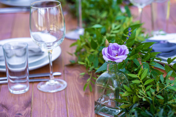 Beautifully decorated wooden table in a summer open-air cafe. Green branch and fresh flowers table decoration
