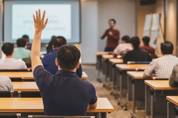 Rückansicht des Publikums in erhobener Hand zur Beantwortung der Frage im Besprechungsraum oder Konferenzsaal über asiatische Sprecher auf der Bühne, Seminargeschäft und Bildungskonzept © THANANIT