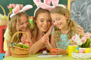 Mother with daughters wearing rabbit ears decorating Easter eggs