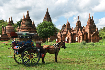 Horse drawn carriage tourists is driving along in front of the ancient temple of Bagan, Myanmar.  - obrazy, fototapety, plakaty