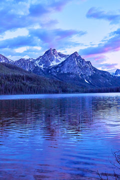 Purple mountain majesty jutting out of blue glacial lake with blue and purple sky