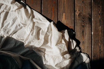 Crumpled cotton fabric milky white on the dark old wooden floor with hard bright shadows.