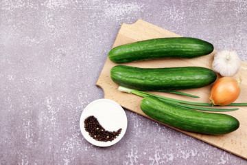 Smooth cucumbers with onions and garlic on a wooden board on a dark wooden background. Top view, flat lay