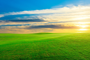 Green grass field and colorful sky clouds at sunset.