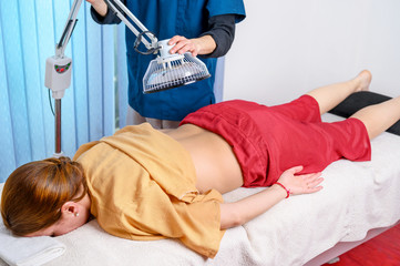 Therapist doing healing infrared treatment on woman back . Alternative medicine, physiotherapy,...