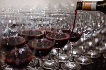 The bartender is pouring red wine in glasses and many empty glasses on the bar counter. Blurred background. wine, tasting, pour, bartender, beverage, dinner concept.