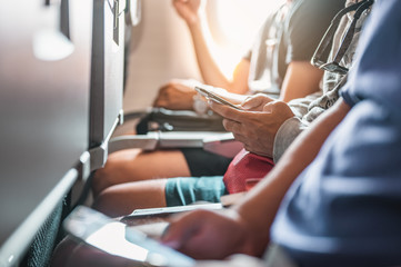 The tourists who are playing the phone and have a ticket on hand on the plane that is preparing to take-off. Airplane, Travel, Smartphone, Airport, ticket, technology concept.