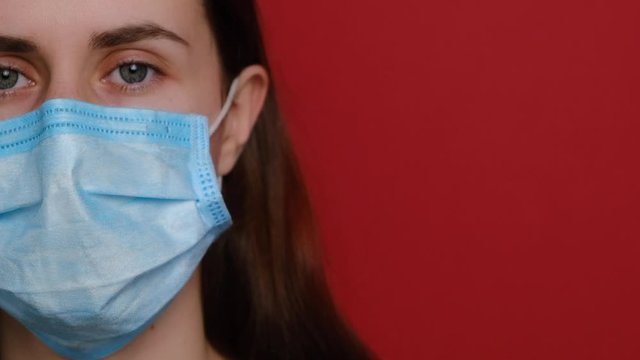 Pandemic, cropped portrait of European young woman wearing protective mask on red background. Female takes off a protective medical mask. Concept health and safety, N1H1 coronavirus, virus protection