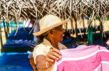 woman salesman on beach trades with a tourist in a hat and bikini on the shore of the sandy ocean among gazebos and sunbeds. Sri Lanka Asia
