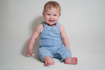  emotional portrait of a one-year-old baby in denim overalls on a uniform light background