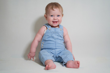  emotional portrait of a one-year-old baby in denim overalls on a uniform light background