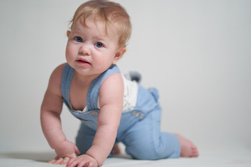 Fototapeta premium emotional portrait of a one-year-old baby in denim overalls on a uniform light background