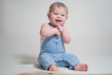 Naklejka premium emotional portrait of a one-year-old baby in denim overalls on a uniform light background