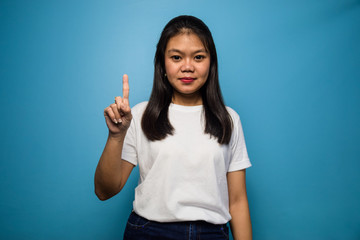 Portrait of Young beautiful asian women using white T-shirt with blue isolated background, one sign, 1